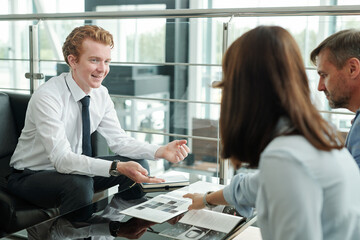 Poster - Happy young manager sitting in front of couple and looking at female client