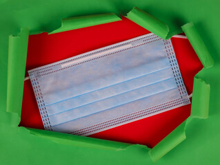 Wall Mural - 
A medical mask lies in the middle on a red background from above with green torn paper around the edges, a close-up top view 