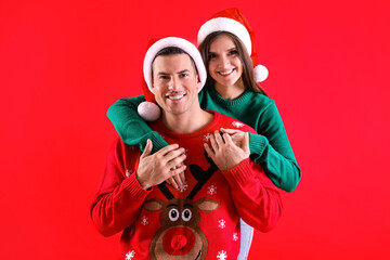 Wall Mural - Beautiful happy couple in Santa hats and Christmas sweaters on red background