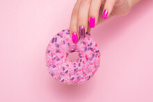 Female hand with pink manicure nails holding strawberry donut