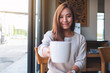 © Farknot Architect - Closeup image of a beautiful young asian woman holding and giving a cup of hot coffee in cafe