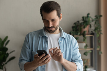 Wall Mural - young caucasian man stand look at smartphone screen browse surf wireless internet on gadget. serious