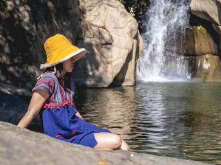 Wall Mural - Women wear traditional Thai costumes and yellow hats. Sitting by the waterfall