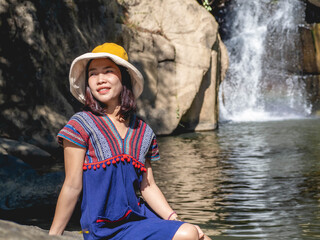 Wall Mural - Women wear traditional Thai costumes and yellow hats. Sitting by the waterfall