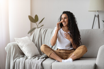 happy young woman sitting on couch, talking on phone