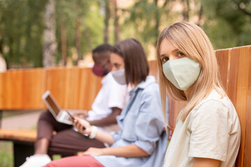 Poster - Young blond woman in protective mask looking at you against two millennials