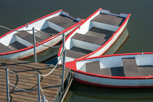 Rowboats Are Moored At The Pier. Boats Made Of Wood With A Red Stripe Along The Top Of The Side. Hemp Ropes Guard The Boat Pier On A Summer Day.