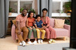 © pressmaster - Happy young African family of father, mother, son and daughter watching tv set
