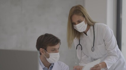 Wall Mural - Medical couple doctors with protective medical facial masks talking and using computer in the office