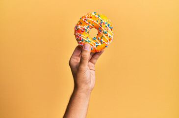 Wall Mural - Hand of hispanic man holding donut over isolated yellow background.