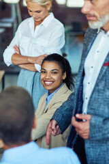 Wall Mural - Young cheerful mixed race woman, female office worker smiling at camera while having a meeting with colleagues