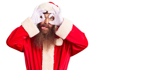 Sticker - Handsome young red head man with long beard wearing santa claus costume doing ok gesture like binoculars sticking tongue out, eyes looking through fingers. crazy expression.