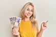 Beautiful caucasian blonde girl holding 5000 japanese yen banknotes smiling happy pointing with hand and finger to the side