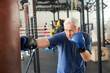 © DenisProduction.com - Senior man hitting punching bag in boxing studio. Old man in gloves beats punching bag in gym.