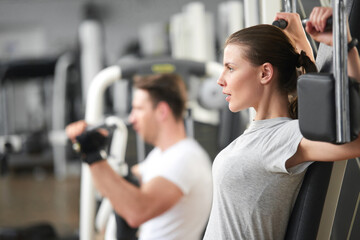 Wall Mural - Confident young woman training at gym. Young determined woman at the sport gym doing arms exercises on a machine. Strength and muscular training.