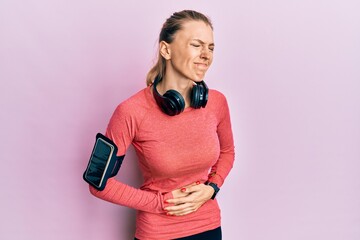 Canvas Print - Beautiful caucasian woman wearing sportswear and arm band with hand on stomach because indigestion, painful illness feeling unwell. ache concept.