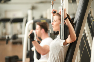 Wall Mural - Pretty slim woman doing chest exercise at gym. Young sexy woman training arms on machine at fitness center, side view.