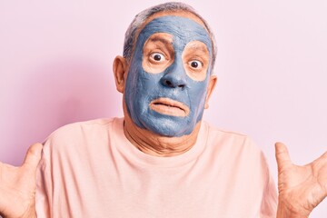 Canvas Print - Senior man with grey hair wearing mud mask clueless and confused with open arms, no idea and doubtful face.