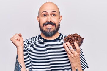 Poster - Young handsome man holding chocolate cereals screaming proud, celebrating victory and success very excited with raised arm