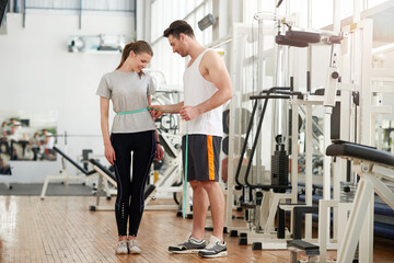 Wall Mural - Personal trainer measuring a woman waist at the fitness club. Fitness instructor checking results. People, sport, fitness and weight loss concept.