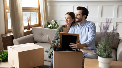 Wall Mural - Dreamy happy man and woman renters unpack boxes moving in together look in distance dreaming thinking. Smiling couple tenants imagine visualize bright future, relocate to own new home. Rent concept.