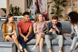 © Kostiantyn - All you need is friends. Group of happy young multicultural people in casual wear looking at smartphone, enjoying time together while sitting on the sofa in the living room