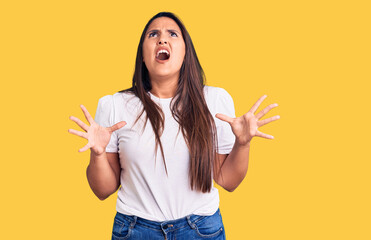 Wall Mural - Young beautiful brunette woman wearing casual t-shirt crazy and mad shouting and yelling with aggressive expression and arms raised. frustration concept.