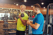 © Kostiantyn - Positive mature man in sportswear doing weight exercises with his young personal trainer, working out at gym with fitness instructor
