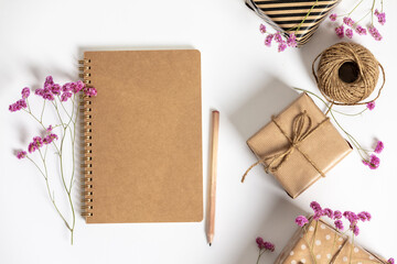 Wall Mural - gift box wrapped in kraft paper, notebook and pink flowers on white background. flat lay styling.