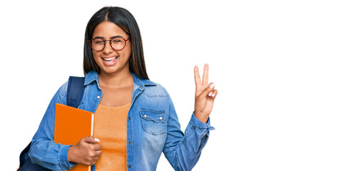 Sticker - Young latin girl wearing student backpack and holding books smiling with happy face winking at the camera doing victory sign with fingers. number two.