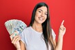 © Krakenimages.com - Young brunette woman holding dollars smiling happy pointing with hand and finger to the side