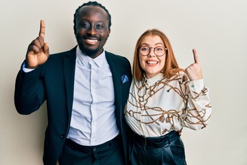 Wall Mural - Young interracial couple wearing business and elegant clothes smiling amazed and surprised and pointing up with fingers and raised arms.