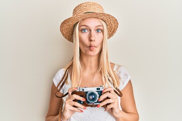 Poster - Young blonde girl wearing summer hat using camera making fish face with mouth and squinting eyes, crazy and comical.