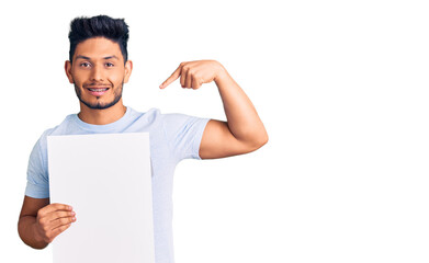 Wall Mural - Handsome latin american young man holding cardboard banner with blank space pointing finger to one self smiling happy and proud