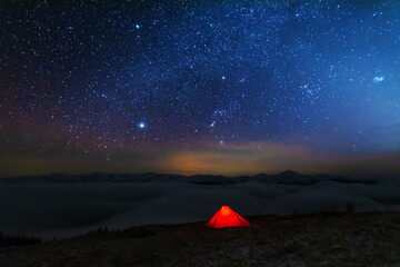 Wall Mural - space starry nights with a bright milky way on the backdrop of tourists with tents.