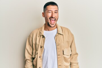 Canvas Print - Handsome man with tattoos wearing casual brown denim jacket winking looking at the camera with sexy expression, cheerful and happy face.