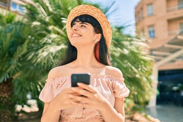 Young hispanic tourist girl wearing summer style using smartphone at the park.