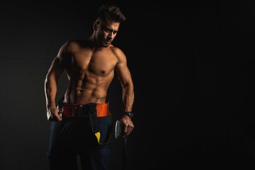 Wall Mural - young handsome adult, muscular firefighter in uniform holding ax of fire equipment in his hands, pensive, isolated on dark background. Low key. Protection concept. there is a place for an inscription