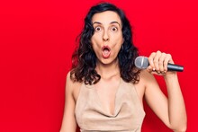 Young Beautiful Hispanic Woman Singing Song Using Microphone Scared And Amazed With Open Mouth For Surprise, Disbelief Face