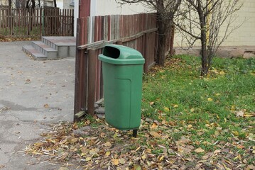 Wall Mural - one green plastic trash can stands in the grass outside by a brown wooden fence