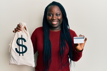 Sticker - Young black woman with braids holding dollars bag and credit card smiling with a happy and cool smile on face. showing teeth.