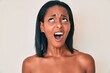 Young african american woman standing topless showing skin angry and mad screaming frustrated and furious, shouting with anger looking up.