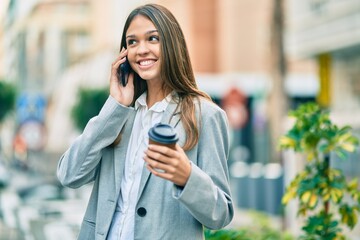 Young latin businesswoman talking on the smartphone drinking coffee at the city.