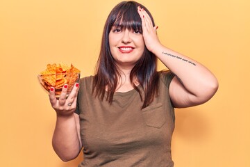 Sticker - Young plus size woman holding nachos potato chips stressed and frustrated with hand on head, surprised and angry face