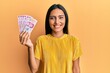© Krakenimages.com - Young brunette woman holding 50 mexican pesos banknotes looking positive and happy standing and smiling with a confident smile showing teeth