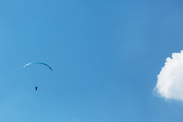 Blue Paraglider flying into the sky with clouds on a sunny day