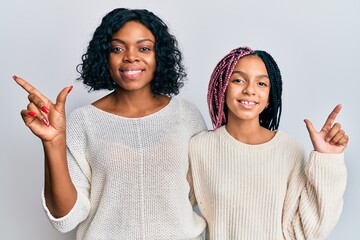 Poster - Beautiful african american mother and daughter wearing casual clothes and hugging cheerful with a smile on face pointing with hand and finger up to the side with happy and natural expression