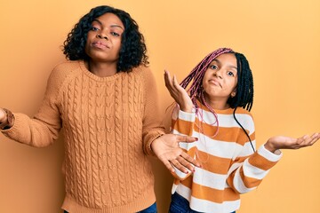 Poster - Beautiful african american mother and daughter wearing wool winter sweater clueless and confused expression with arms and hands raised. doubt concept.