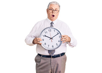 Canvas Print - Senior grey-haired man wearing business clothes and holding clock scared and amazed with open mouth for surprise, disbelief face