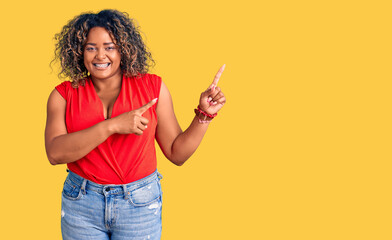 Young african american plus size woman wearing casual style with sleeveless shirt smiling and looking at the camera pointing with two hands and fingers to the side.